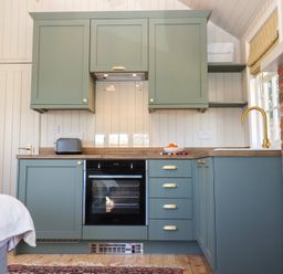 A kitchen with green cabinets a black oven a toaster a bowl of oranges and a gold faucet at The Woodshed in Tendring near Weeley