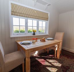 A small dining area with a wooden table and two chairs near a window with a patterned blind at The Woodshed in Tendring near Weeley