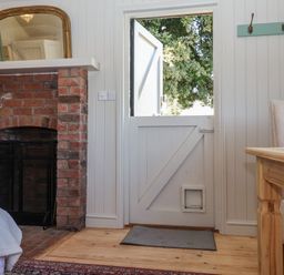 An interior room with a half open wooden door a brick fireplace and a wooden table with a chair at The Woodshed in Tendring near Weeley