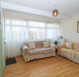 A living room with two sofas covered in throws a large window with vertical blinds and sheer curtains a green wall with a beach picture and a wooden floor at Chalet 469 Newport Norfolk