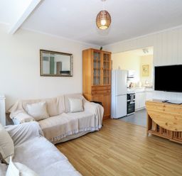 A living room with two sofas a wooden cabinet a wall-mounted TV and an open doorway to a kitchen at Chalet 469 in Newport Norfolk