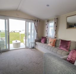 A living room with a large sofa and sliding glass doors leading to an outdoor seating area at Breathing Space in Happisburgh near Walcott