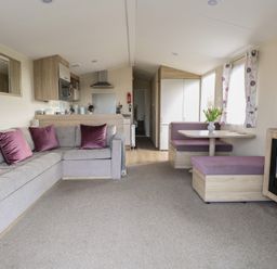 A living area with a grey sofa with purple pillows a dining nook with purple seating a kitchen area and a wall-mounted electric fireplace at Breathing Space in Happisburgh near Walcott