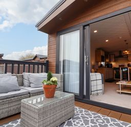 A patio with wicker furniture and a potted plant outside a living room with a coffee table and kitchen at Lodge 36 - Kingfisher Lodge in Wickhamford near Evesham