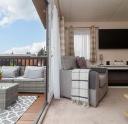 A living room with a gray armchair next to a fireplace and a wall-mounted TV at Lodge 36 - Kingfisher Lodge in Wickhamford near Evesham