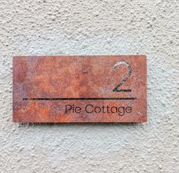 A house number plaque with number 2 and text Pie Cottage on a textured wall at Pie Cottage in Teignmouth
