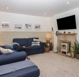 A living room with blue sofas, a wall-mounted TV above a fireplace, lamps, artwork above the sofa, and a plant near the fireplace at Pie Cottage in Teignmouth