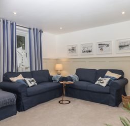A living room with two navy blue sofas a small round table between them striped curtains and framed pictures on the wall at Pie Cottage in Teignmouth