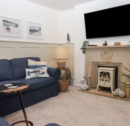 A living room with blue sofas a small metal side table a lamp on a round side table and a fireplace with decorations at Pie Cottage in Teignmouth