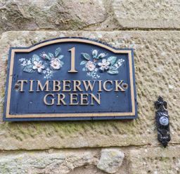 A house number plaque with floral decoration and the name Timberwick Green mounted on a stone wall at Timberwick Green Akeld near Wooler