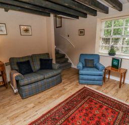 A living room with a sofa and armchair a red patterned rug wooden side tables and a window at Timberwick Green in Akeld near Wooler