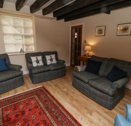 A living room with plaid sofas and armchairs a red rug and a side table with a lamp at Timberwick Green Akeld near Wooler