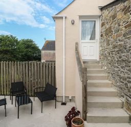 An outdoor patio area with black metal chairs and table next to stone and plaster walls with steps leading to a white door at Sea View Loft in Rosudgeon