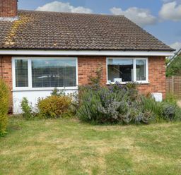 A brick house with two windows and bushes in front with a grassy lawn at Little Lodge in Dersingham