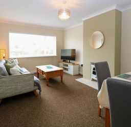 A living room with a sofa a coffee table a TV on a stand a round mirror on the wall and dining chairs at Little Lodge in Dersingham