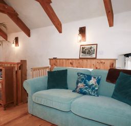 A snug room with a teal sofa and wooden features at Stribleys Barn in Cusgarne near St Day