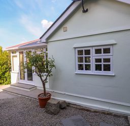 Outside view of a white house with a potted tree nearby and a gravel patio at Little Acorns in Gweek