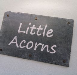 A rectangular stone plaque with the text Little Acorns mounted on a white wall at Little Acorns in Gweek