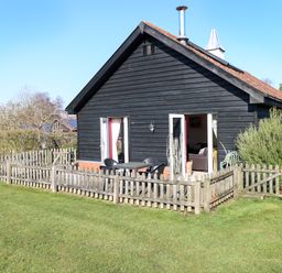 A small black wooden house with a red brick base and a wooden picket fence surrounding a patio area at Swallow Barn in Holton near Halesworth