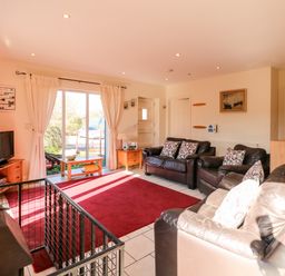 A living room with three leather sofas a red rug a wood stove and sliding glass doors at Swallow Barn in Holton near Halesworth