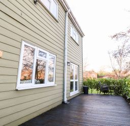An exterior view of a house with beige siding a wooden deck and outdoor table and chairs at Arnside House in South Lakeland Leisure Village