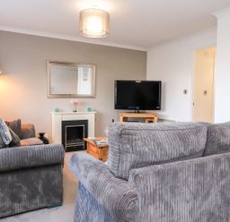 A living room with two grey sofas a fireplace a television on a wooden stand and a floor lamp at Arnside House in South Lakeland Leisure Village