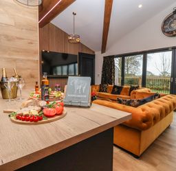 A living room with orange sofas wooden table with food and drinks large clock on wall and doors to garden at Routhorpe Lodge in Bainton near Great Driffield