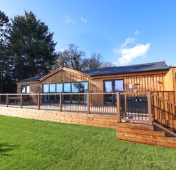 A wooden cabin with large glass windows and a deck with railings on a grassy lawn at Routhorpe Lodge in Bainton near Great Driffield