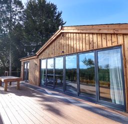 An outdoor wooden deck with a table and large glass sliding doors on a wooden building at Routhorpe Lodge in Bainton near Great Driffield