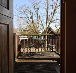 A wooden balcony with a small metal table and two metal chairs with two cups on the table at Woodland Retreat Lodge in Brundish near Laxfield