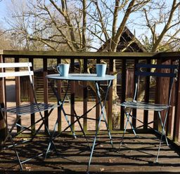 A wooden balcony with two metal chairs and a small round table with two mugs at Woodland Retreat Lodge Brundish near Laxfield