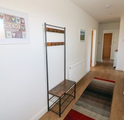 A hallway with a bench and coat rack a radiator a striped rug and framed pictures on the wall at Arfryn in Solva