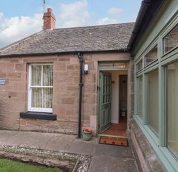 Entrance to a stone cottage with a green door and windows and a tiled roof at Dromore Cottage in Norham
