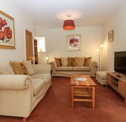 A living room with beige sofas a wooden coffee table a TV on a wooden stand and wall art at Dromore Cottage in Norham