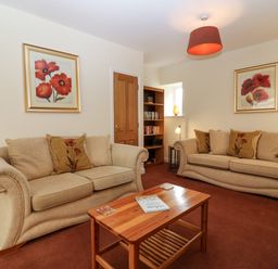 A living room with two beige sofas a wooden coffee table and framed flower pictures on the walls at Dromore Cottage in Norham