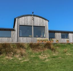 A wooden building with large windows and flower pots on a deck overlooking grass at WildLuing Cullipool Isle Of Luing