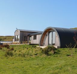 A curved wooden and metal building on a grassy hillside at WildLuing in Cullipool Isle Of Luing
