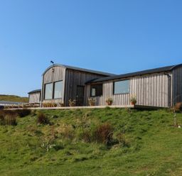 A wooden cabin with large windows and flower pots on a deck in a grassy area at WildLuing in Cullipool Isle Of Luing