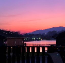 A lake with houses and hills in the background at sunset at Sunset Retreat South Lakeland Leisure Village near Carnforth