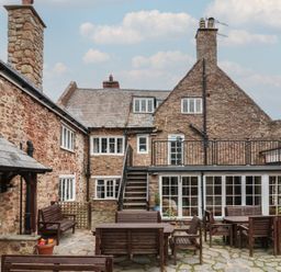 An outdoor stone courtyard with wooden tables and benches in front of a stone building at Dragon House in Bilbrook near Minehead