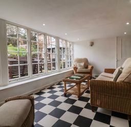 A sitting room with wicker furniture and large windows overlooking a garden at Dragon House in Bilbrook near Minehead