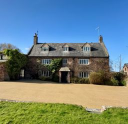 A stone house with ivy on the walls and a gravel driveway in front at Dragon House in Bilbrook near Minehead