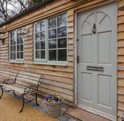 An exterior view of a wooden cottage with three windows a bench and a door labeled Gatekeepers Cottage at Bilbrook near Minehead