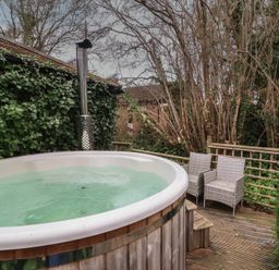 An outdoor hot tub on a wooden deck with two wicker chairs surrounded by trees and ivy at Gatekeeper's Cottage in Bilbrook near Minehead
