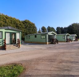 Four green mobile homes with steps on a gravel area near trees at Lodge 2 in Silverdale
