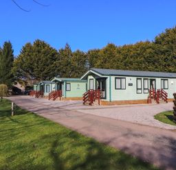 A row of green lodges with red railings next to a gravel driveway and green lawn at Lodge 3 in Silverdale