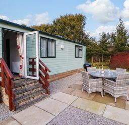 An outdoor patio with a round table and four chairs next to a small building with open door and steps at Lodge 4 in Silverdale
