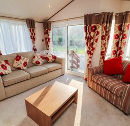 A living room with two sofas a wooden coffee table and floral curtains at Lodge 4 in Silverdale