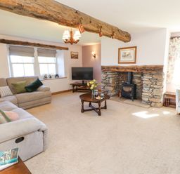 A living room with beige sofas a stone fireplace a wooden coffee table and a TV at High Wood Foot in Bampton Cumbria