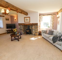 A living room with a stone fireplace a wood stove two sofas a television and wooden beams at High Wood Foot in Bampton Cumbria